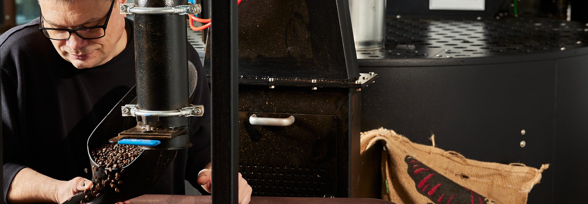 Palacz kawy wsypujący świeżo palone ziarna do pojemnika w kawiarni, pokazujący rzemieślniczą produkcję kawy.