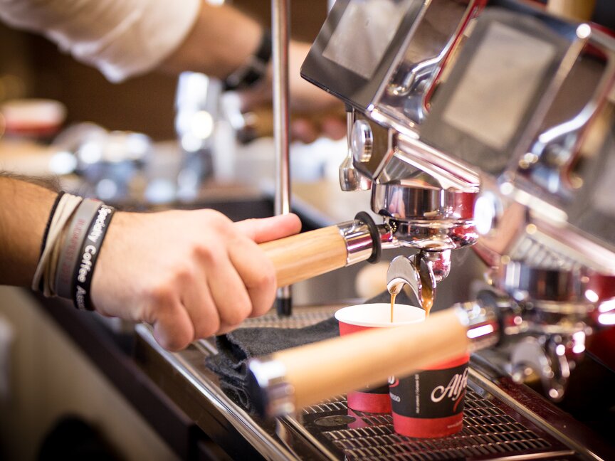 Barista przygotowujący espresso, ze świeżo zaparzoną kawą nalewaną do dwóch czerwonych filiżanek w kawiarni.