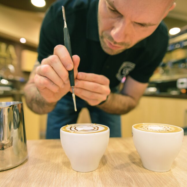 Barista tworzący skomplikowane latte art na filiżankach kawy w kawiarni. Idealny dla entuzjastów kawy i szkolenia baristów.