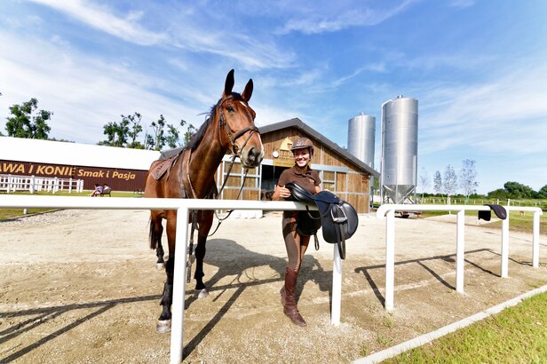 Jeździec pozuje z koniem w stajni, gotowy do sesji jeździeckiej w malowniczej wiejskiej scenerii.