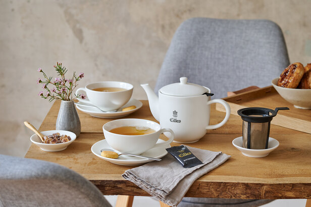 Elegantes Teeservice von Eilles auf einem Holztisch mit Teetassen, einer Teekanne und Snacks für einen herrlichen Nachmittagstee.