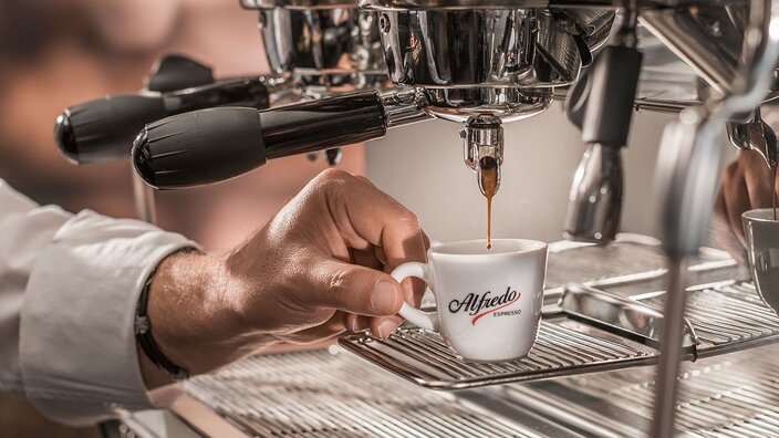 A hand pours rich espresso into an elegant Alfredo cup from a polished coffee machine. Perfect for coffee lovers.