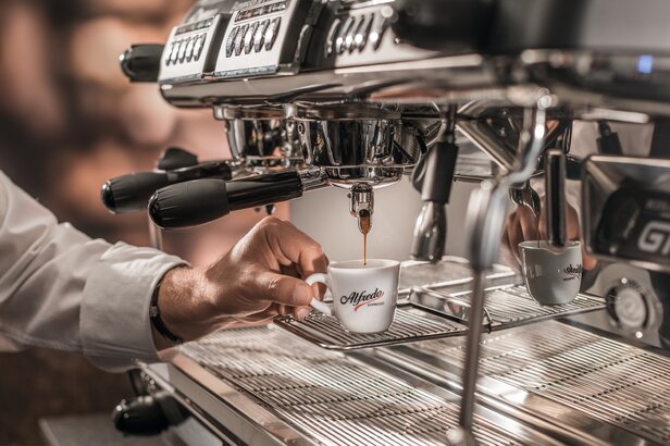 Barista gießt frisch gebrühten Espresso in eine elegante Alfred-Kaffeetasse an einer eleganten Espressomaschine.
