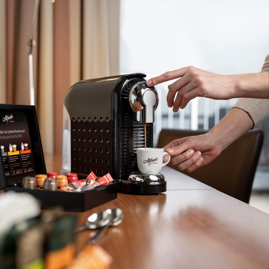 Un utilisateur prépare un expresso avec une machine à café Alfredo, mettant en valeur des capsules de café et une cuisine moderne.