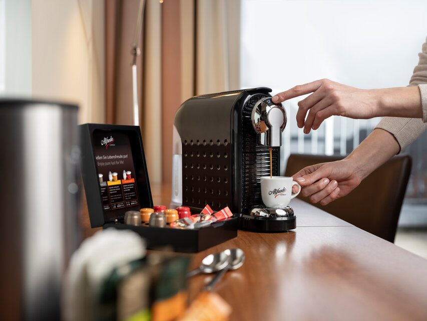 A user brews espresso with an Alfredo coffee machine, showcasing coffee capsules and a modern kitchen setting.