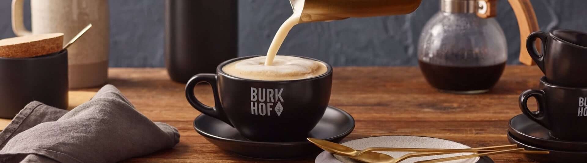 Pouring velvety milk into a cappuccino in a stylish café setting with Burkhof accessories.