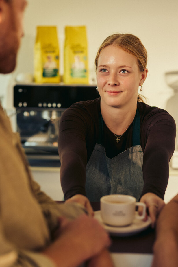 Barista serving coffee with a smile at Café Intención, highlighting a warm café atmosphere.
