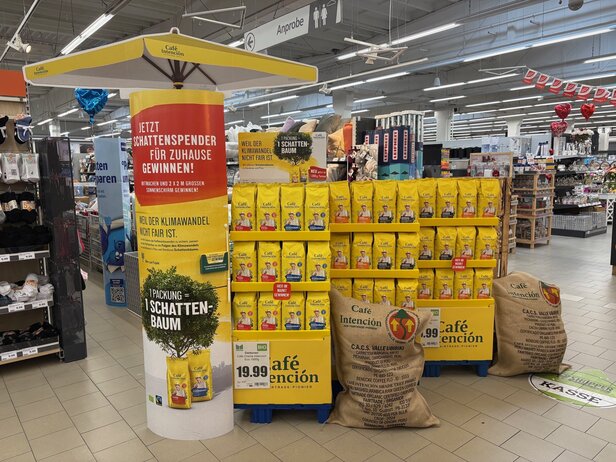 Promotiedisplay voor Café Intención met fairtrade koffietassen en een wedstrijd voor een tuinparaplu in de winkel.