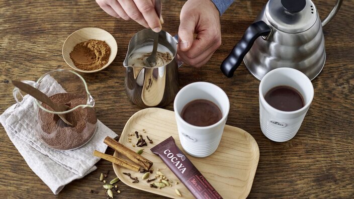 Heerlijke Cocaya chocoladedrankjes met verse kruiden en cacao bereiden op een rustieke houten tafel. Perfect voor gezellige momenten.