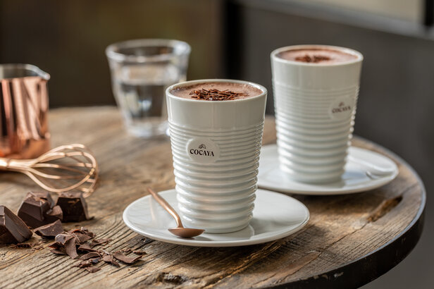 Rijke cacaodranken geserveerd in stijlvolle kopjes, vergezeld van pure chocolade en een garde op een rustieke houten tafel.
