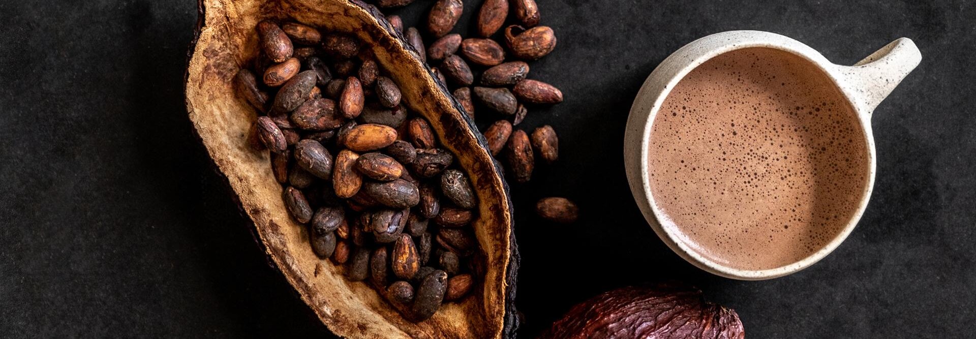 Cacaobonen en een kop rijke chocolade drinken op een donker oppervlak en tonen de essentie van fijne chocolade.