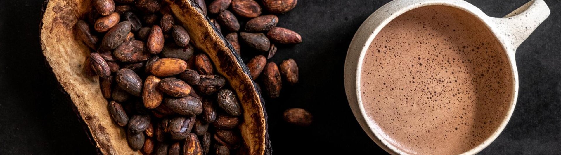 Des fèves de cacao et une tasse de chocolat riche boivent sur une surface sombre, mettant en valeur l'essence du chocolat fin.