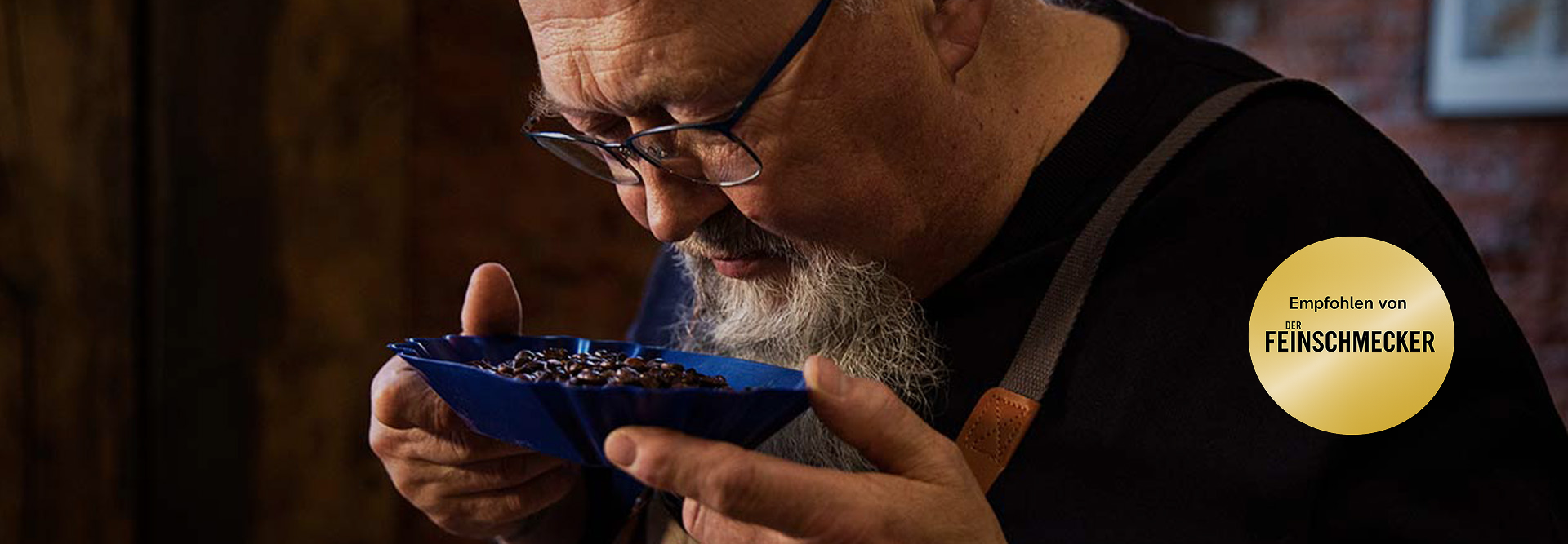 Expert coffee taster evaluates aromatic beans in a blue dish, showcasing Eilles Kaffee's mastery in roasting.