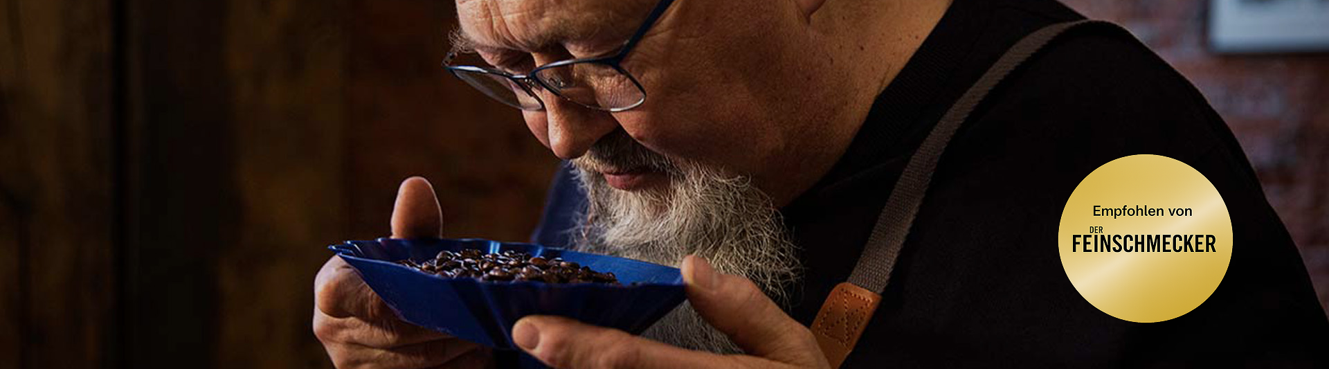 Ein fachkundiger Kaffeeverkoster bewertet die aromatischen Bohnen in einer blauen Schale, die das meisterhafte Röstverfahren von Eilles Kaffee zeigt.
