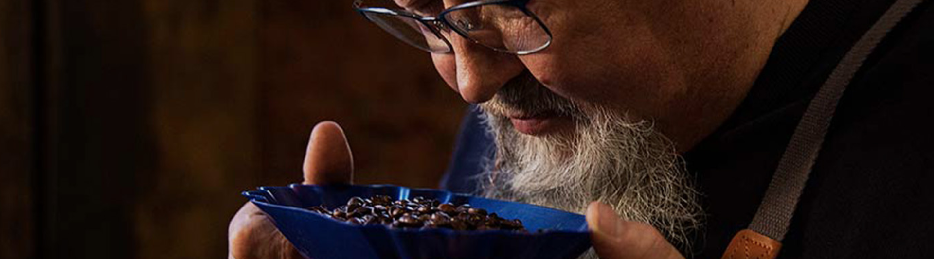 Un expert en dégustation de café évalue les grains aromatiques dans un plat bleu, mettant en valeur la maîtrise de la torréfaction d'Eilles Kaffee.