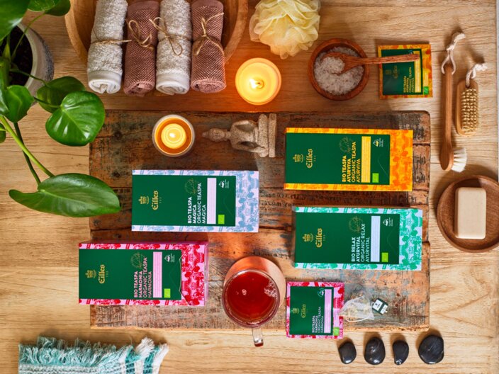 Relaxation essentials display with EILLES tea, candles, herbs, and spa accessories on a wooden tabletop. Ideal for self-care.