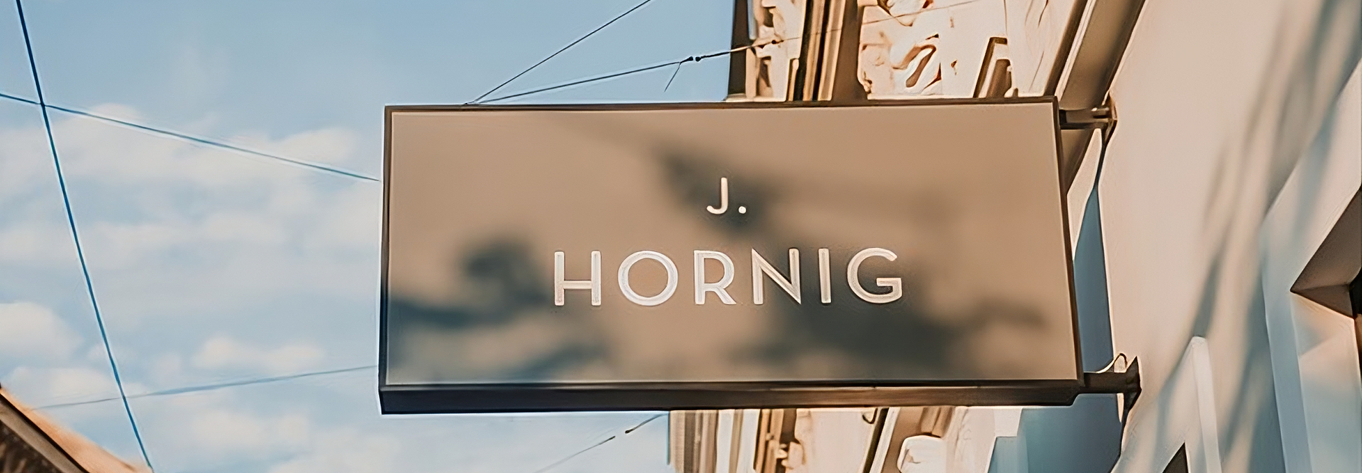 Sign for J. Hornig hanging outside a stylish building against a blue sky, showcasing branding and urban architecture.