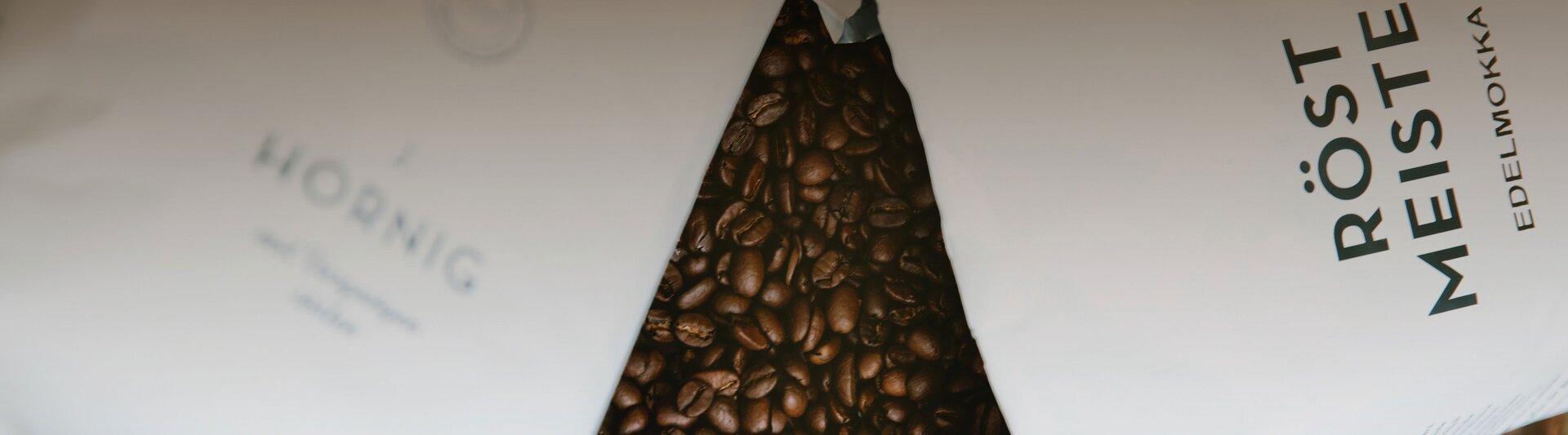 Premium coffee beans spill from Röstmeister and J. Hornig packaging, showcasing rich flavours and quality roasting.