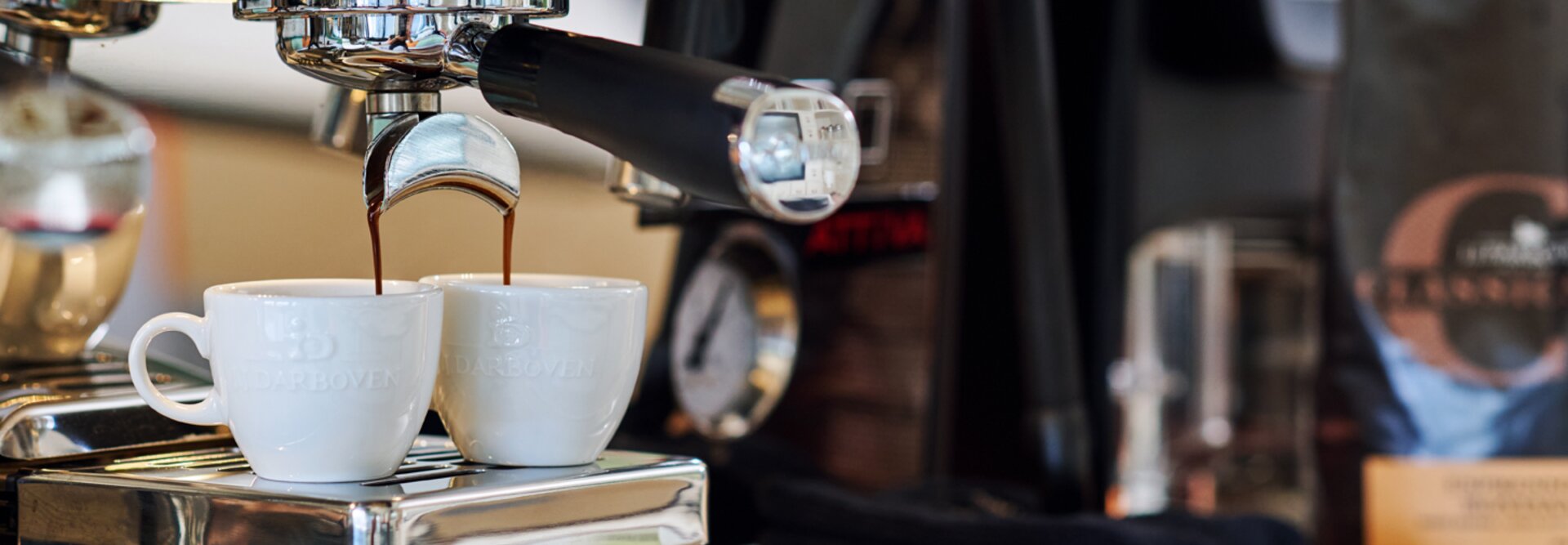 Świeże espresso nalewane do dwóch filiżanek z ekspresu La Cimbali, obok ziarna kawy.