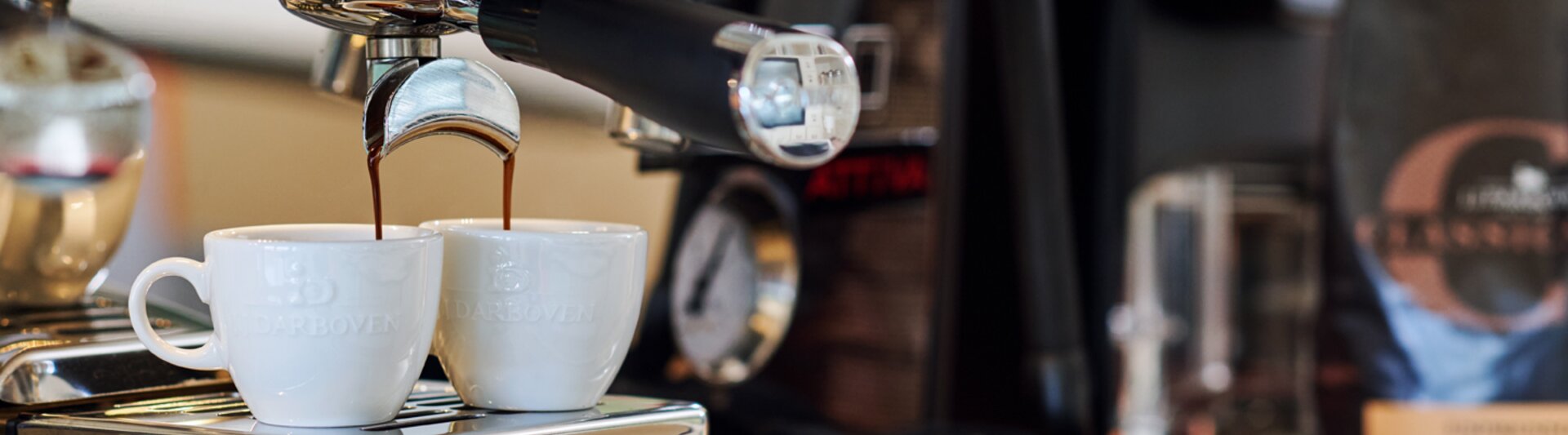 Frischer Espresso in zwei Tassen aus einer La Cimbali Espressomaschine, daneben Kaffeebohnen.