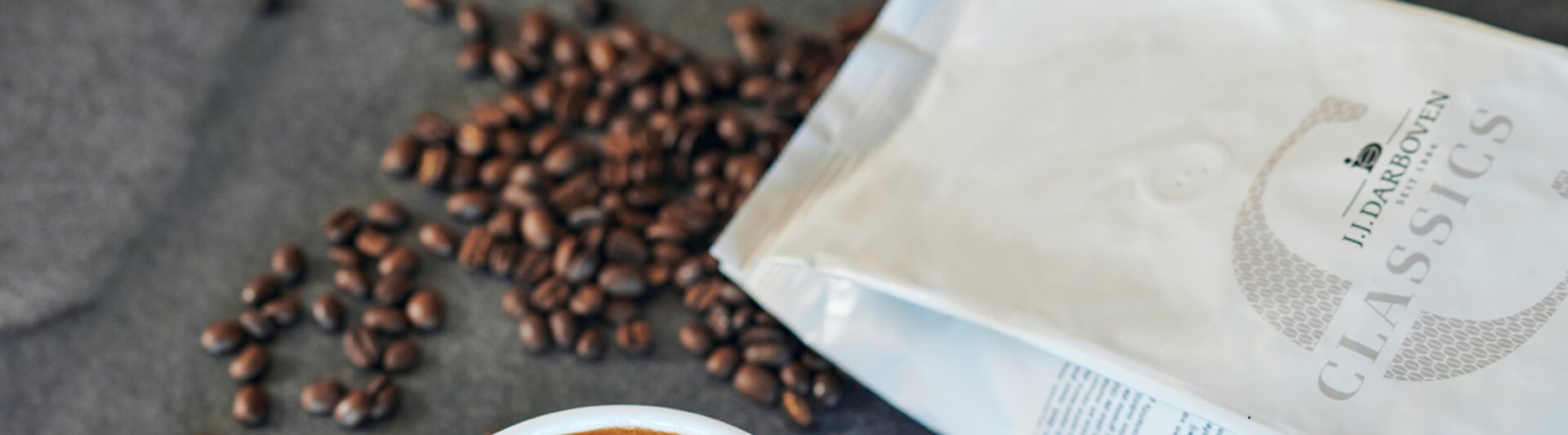 Latte with intricate art design, surrounded by coffee beans and a bag of J.J. Darboven Classics coffee.