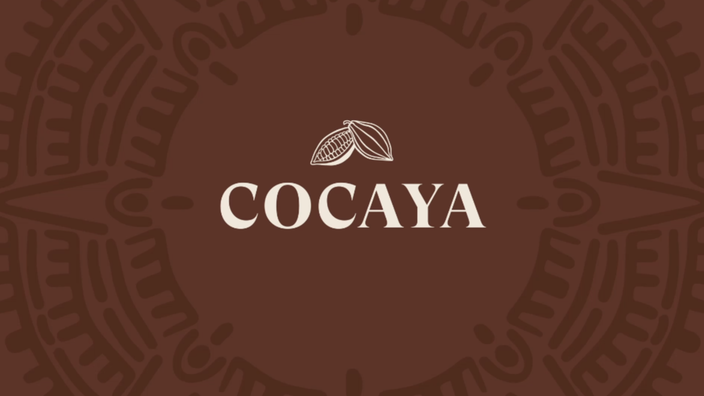 Logo Cocaya s kakaovými bôbmi na sýtom hnedom pozadí, ktoré predstavuje remeselnú výrobu čokolády.