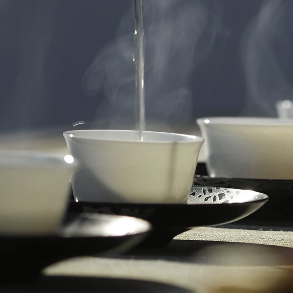 Das dampfende heiße Wasser wird in zarte Tassen gegossen, perfekt für den Teegenuss in einer ruhigen Umgebung.