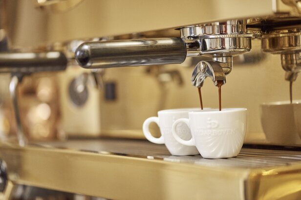 Frisch gebrühter Espresso fließt aus einer professionellen Kaffeemaschine in zwei weiße Tassen, die eine reichhaltige Kaffeemechanik präsentieren.