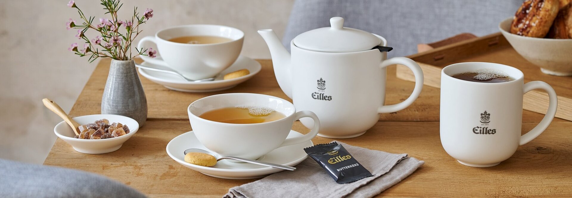 Elegant Eilles theeservies met verschillende soorten thee, koekjes en een vaas bloemen op een rustieke houten tafel.