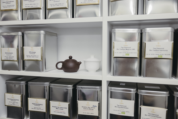 Verschillende theeblikken en keramische theepotten netjes gerangschikt op een plank in een theewinkel.