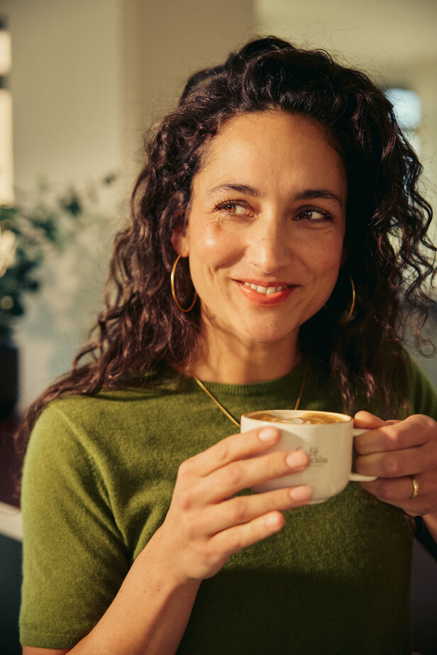 Une femme savoure un café dans un café, rayonnant de chaleur et de joie tout en tenant sa tasse avec un sourire.