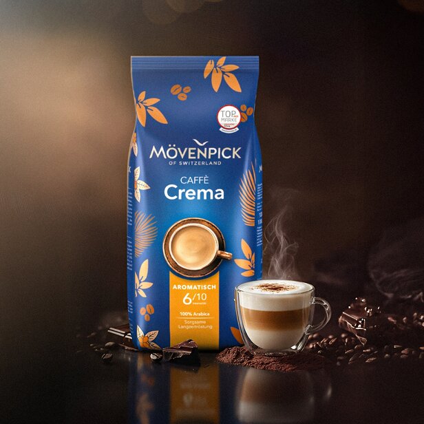Vrecúško kávy Mövenpick Caffè Crema s pariacou sa šálkou cappuccina, ktoré zvýrazňuje jej bohatú arómu a zrná 100 % arabiky.