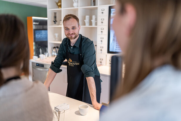 Barista in an apron engaging customers at a modern café, showcasing a welcoming atmosphere and quality service.