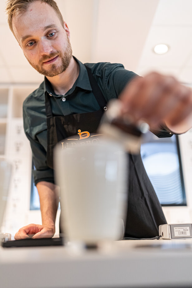 Ein Barista bereitet ein cremiges Getränk zu und zeigt seine Kaffeekünste in einem modernen Café.