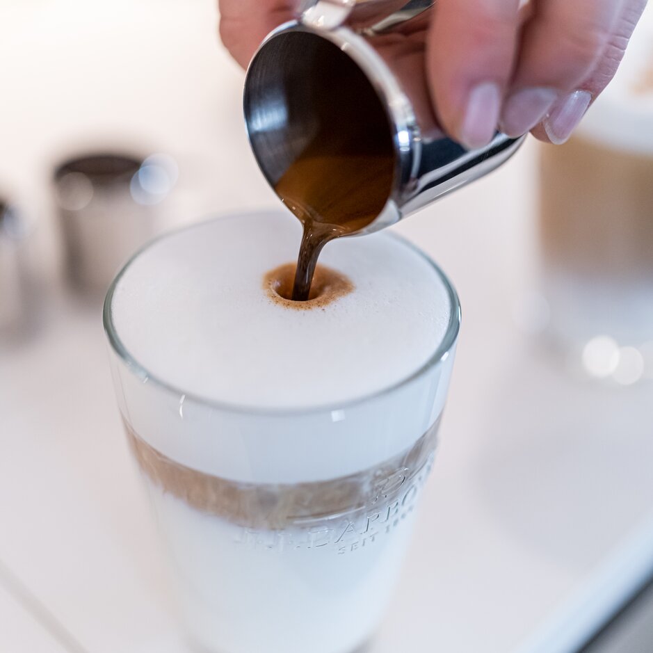 Reichhaltiger Espresso wird in einen schaumigen Milchkaffee gegossen, der die perfekte Kaffeekunst im Glas darstellt.