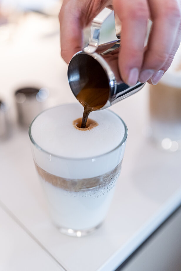 Reichhaltiger Espresso wird in einen schaumigen Milchkaffee gegossen, der die perfekte Kaffeekunst im Glas darstellt.
