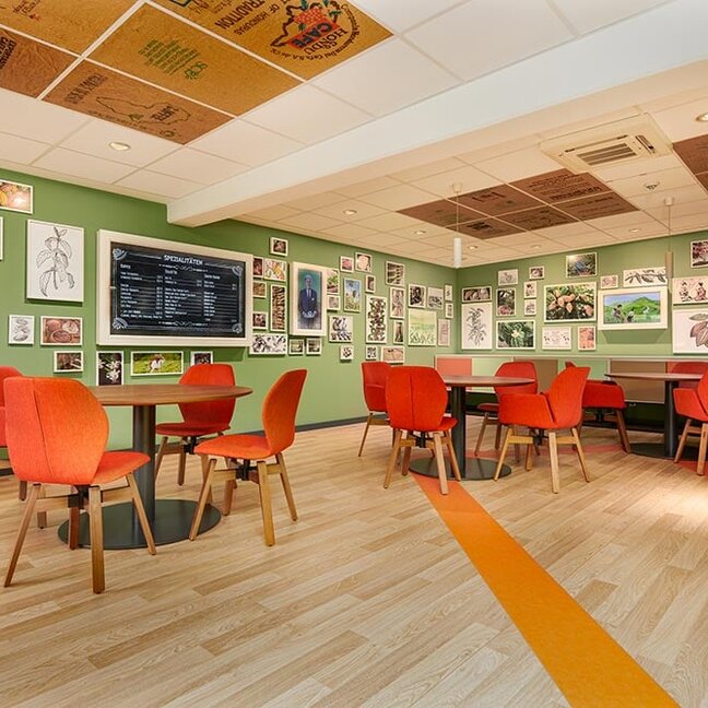 Bright café space with orange chairs and nature-themed art on green walls, ideal for gatherings and relaxation.