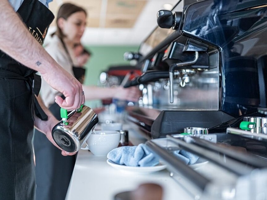 Barista training session with staff using espresso machines and milk frothers to create coffee beverages.