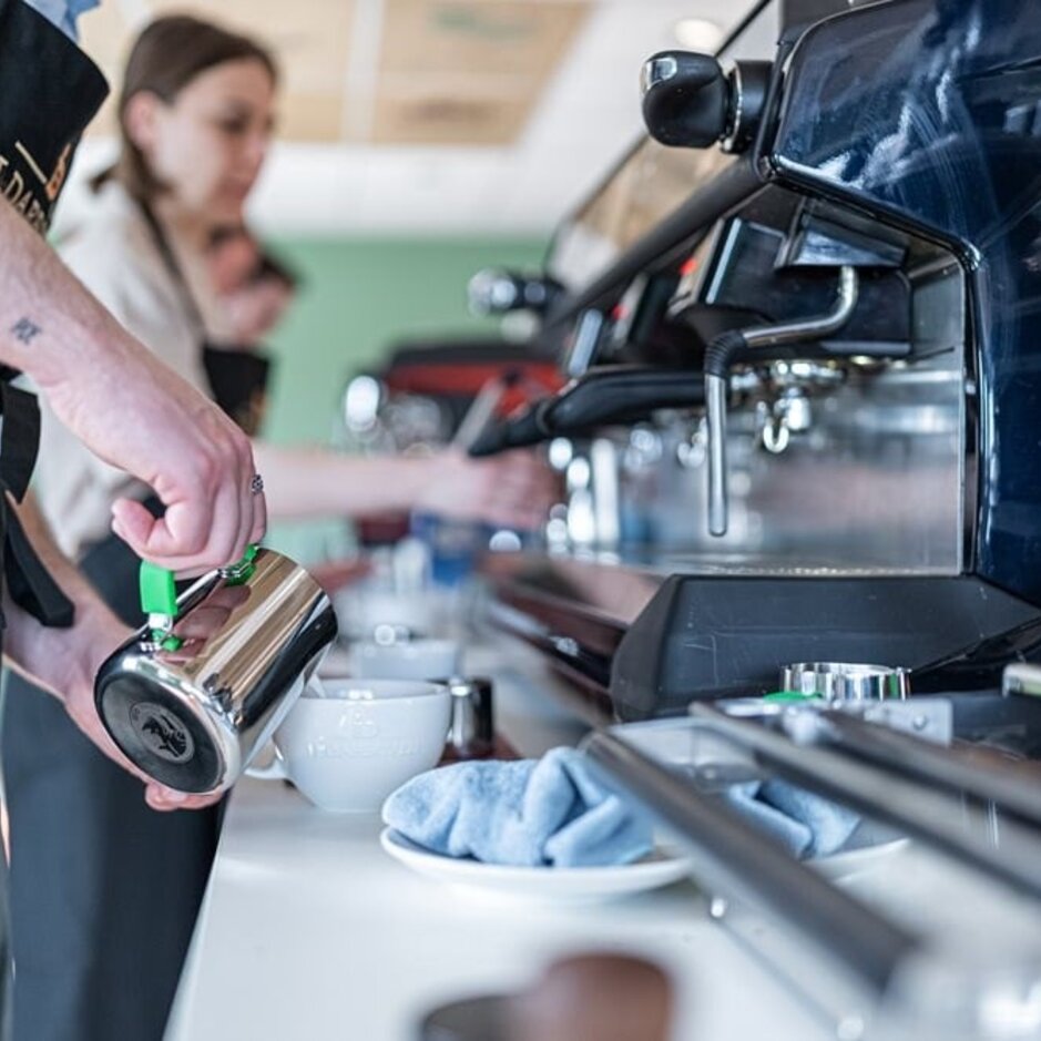 Barista-Schulung mit Mitarbeitern, die Espressomaschinen und Milchaufschäumer zur Zubereitung von Kaffeegetränken verwenden.