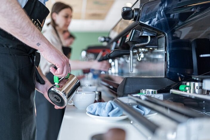 Barista training session with staff using espresso machines and milk frothers to create coffee beverages.