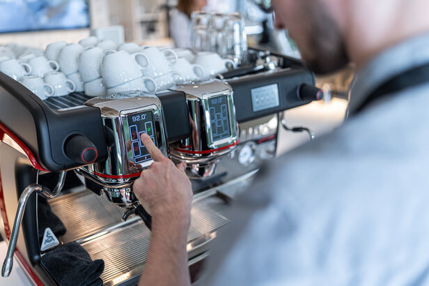 Barista adjusting temperature settings on an espresso machine in a modern coffee academy setting.