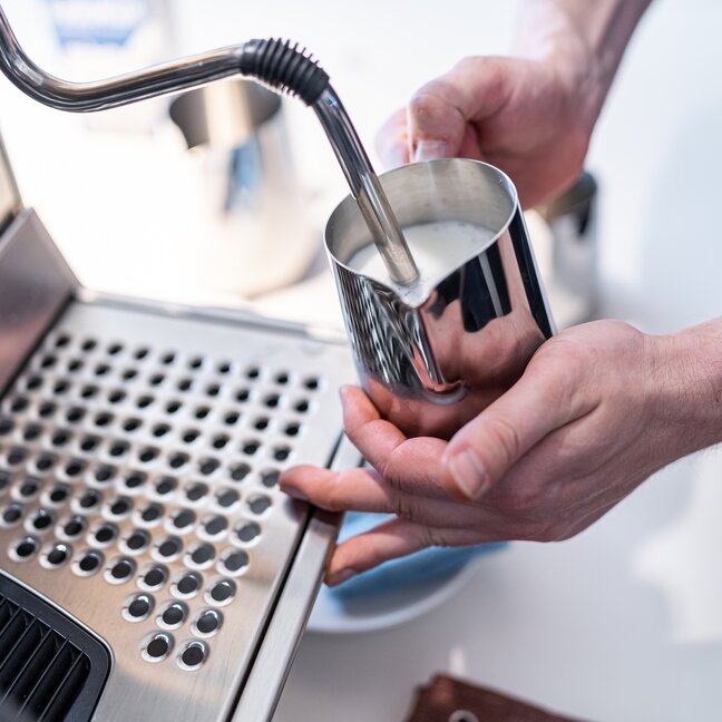 Barista vaporisant du lait dans une cruche en acier inoxydable à l'aide d'une machine à espresso pour une préparation parfaite de la mousse.