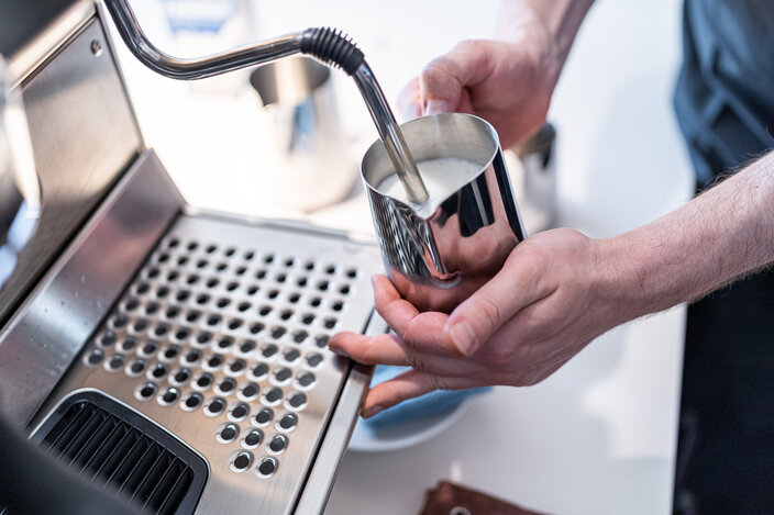 Barista steaming milk in a stainless steel jug using an espresso machine for perfect froth preparation.