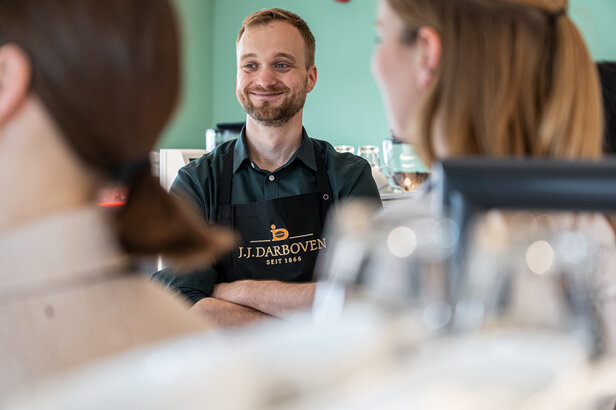 Barista met een glimlach en klantencontact bij J.J. Darboven, een gerenommeerd koffiemerk sinds 1866.