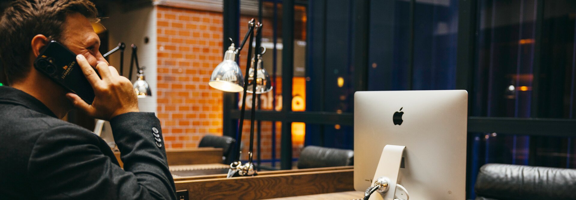 A professional man on the phone at a sleek desk, featuring an Apple computer and a coffee cup in a modern workspace.