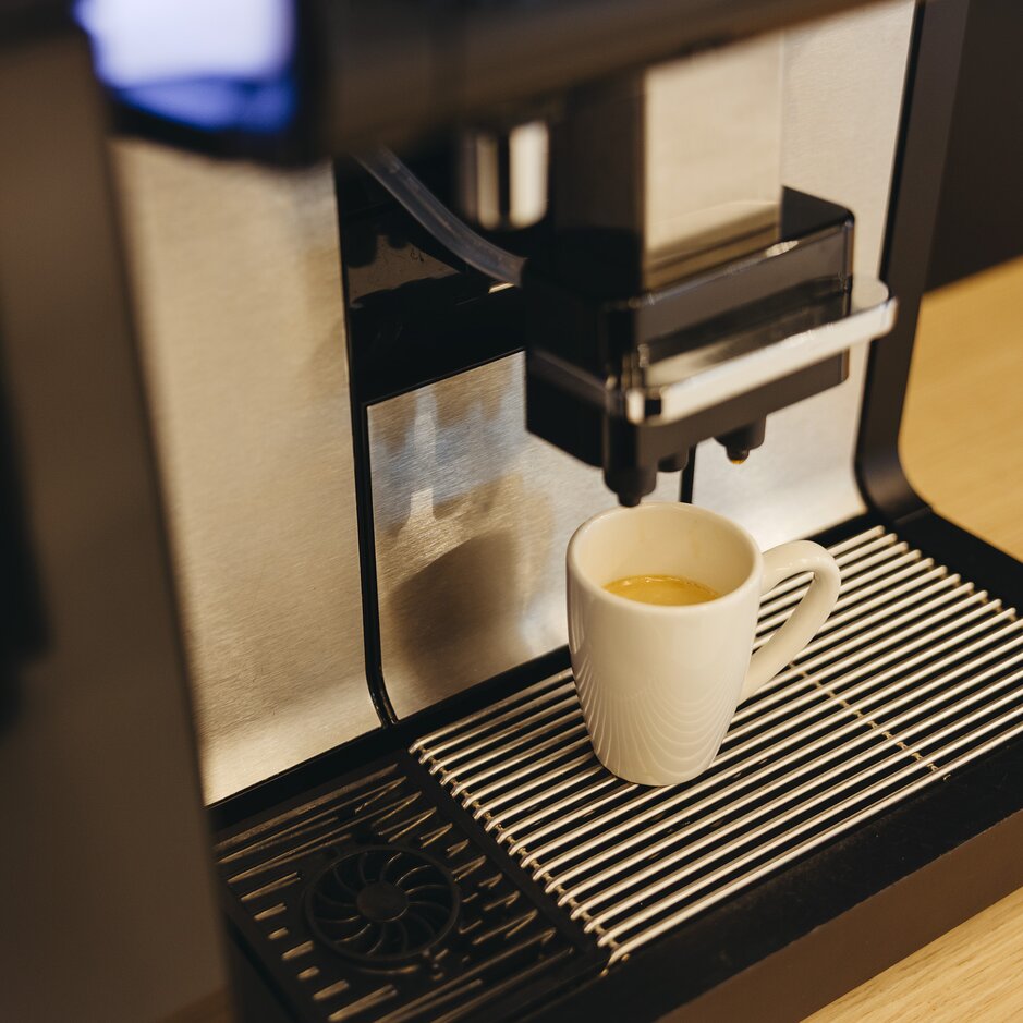 Espressomaschine, die in einer modernen Küche eine Tasse Kaffee zubereitet. Das Design aus rostfreiem Stahl ergänzt eine Holzoberfläche.