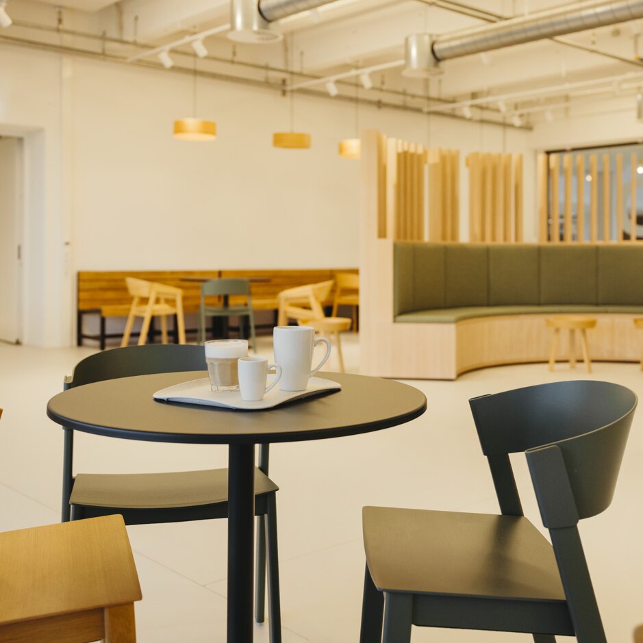 Moderný interiér kaviarne s minimalistickým sedením, okrúhlym stolom na kávu a teplými drevenými akcentmi vytvára príjemnú atmosféru.