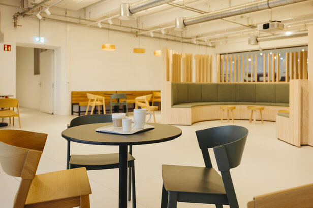 Moderný interiér kaviarne s minimalistickým sedením, okrúhlym stolom na kávu a teplými drevenými akcentmi vytvára príjemnú atmosféru.