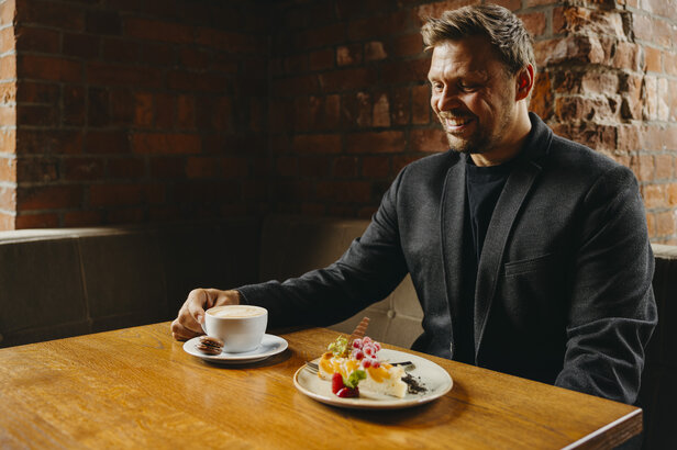 Ein Mann genießt einen Kaffee und ein Dessert in einem gemütlichen Café mit Backsteinwänden, das ein zwangloses Esserlebnis bietet.