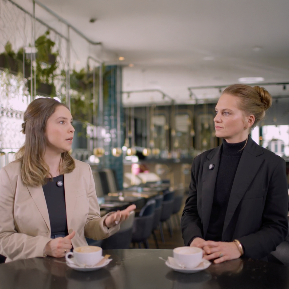 Two women engage in a discussion over coffee in a stylish café setting, showcasing a modern and inviting atmosphere.